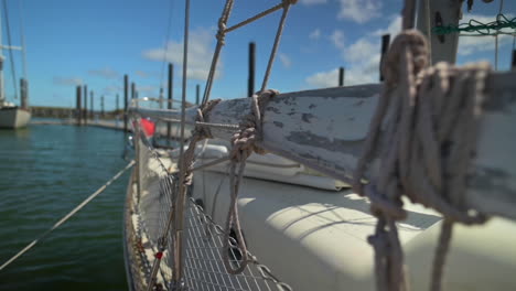 close up of ropes tied on wooden cleat of a sailboat with bright sky and calm waters in background - shallow dof