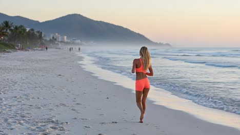 a young woman jogs along a serene beach at sunset, capturing the essence of a peaceful workout with gentle waves and misty mountains in the background.