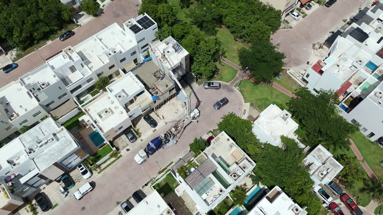 Orbit drone shot of a concrete pump pouring cement to make the tile of a house with several workers spreading the material