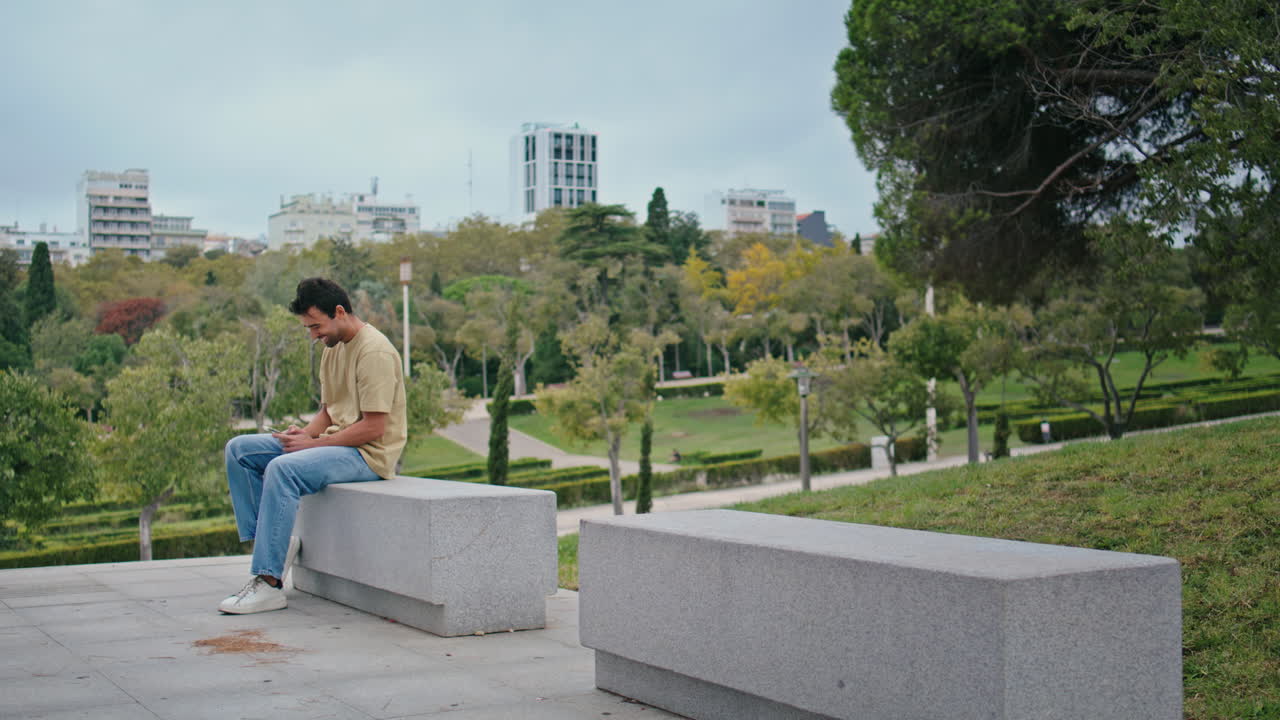 벤치에 앉아 스마트폰으로 소셜미디어를 보는 웃는 남자.