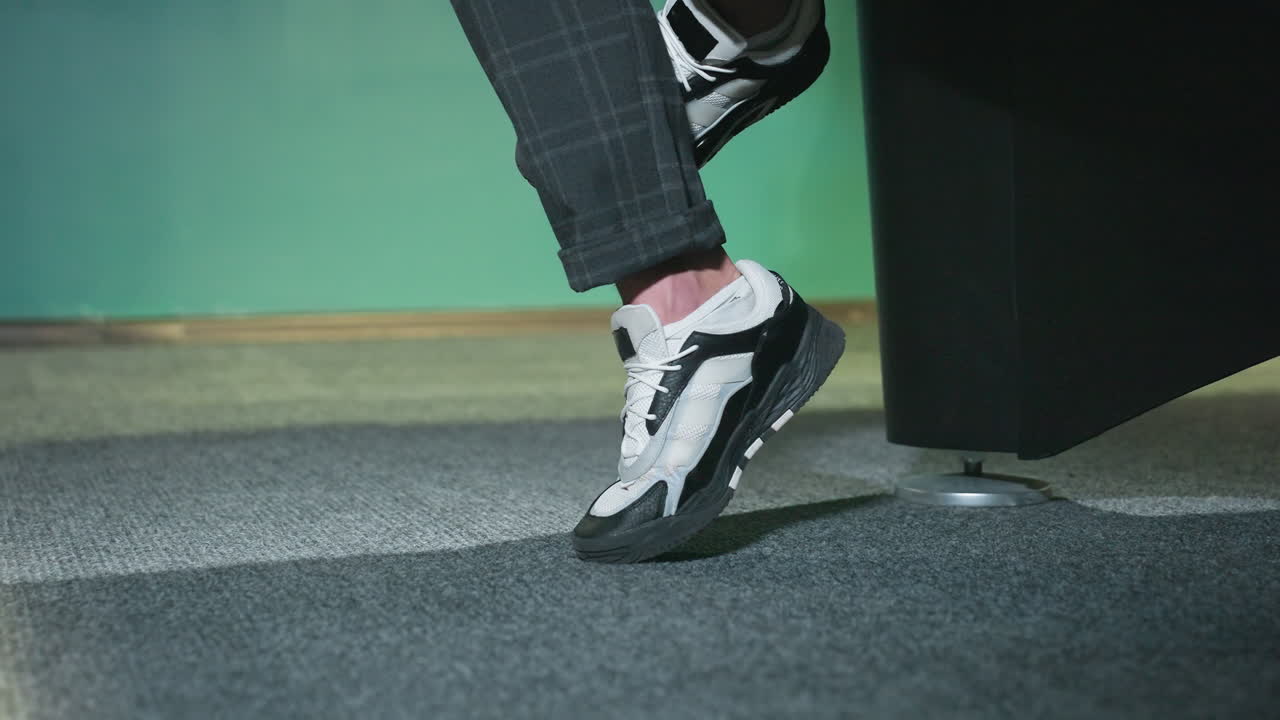 toma de primer plano de una pierna masculina con zapatillas de deporte elegantes blancas y negras con pantalones a cuadros grises. pie ligeramente levantado del piso de alfombra gris, declaración de moda moderna y casual