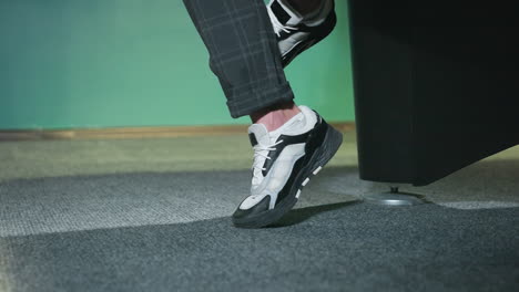 close-up shot of male leg wearing stylish white and black sneakers with grey plaid trousers. foot slightly lifted off grey carpeted floor, modern and casual fashion statement