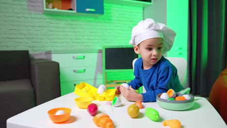 toddler boy in a cook's cap plays at home. baby chef plays with toy food. black cat appears.