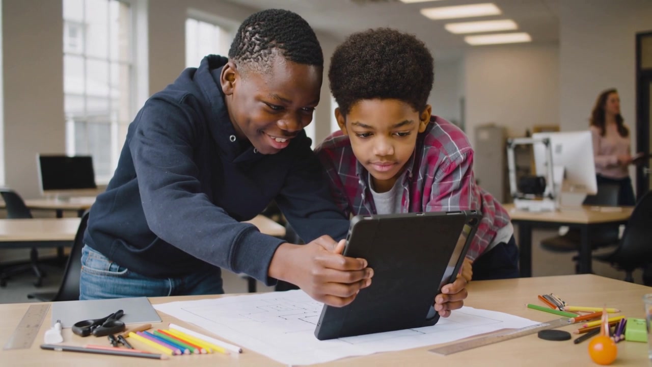 Spotting sketch, teen in navy hoodie and peer in plaid comparing tablet in classroom for project