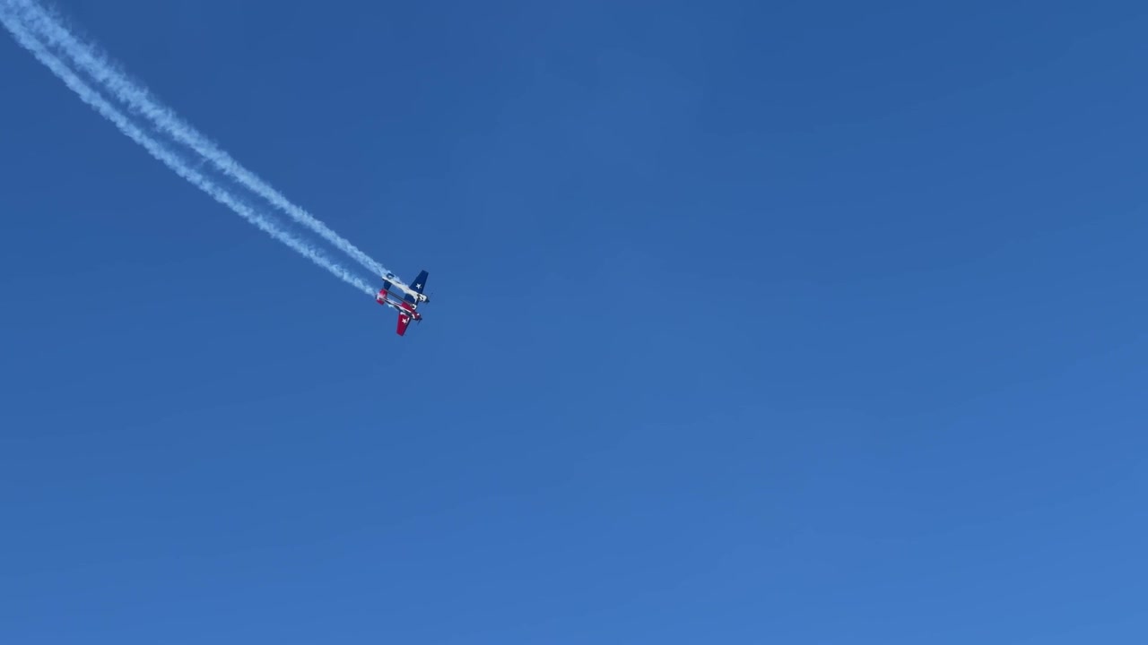 Propeller airplane performs vertical climbs and loops leaving white smoke trails against clear blue sky.