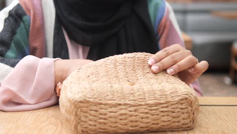 woman with hijab using phone and straw bag in a cafe