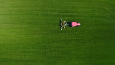 tractor rojo cortando césped en un campo verde - vista aérea de arriba