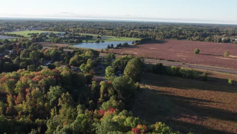 aerial drone forward moving shot over agricultural field beside a highway with the view of a lake in the background on a autumnal evening