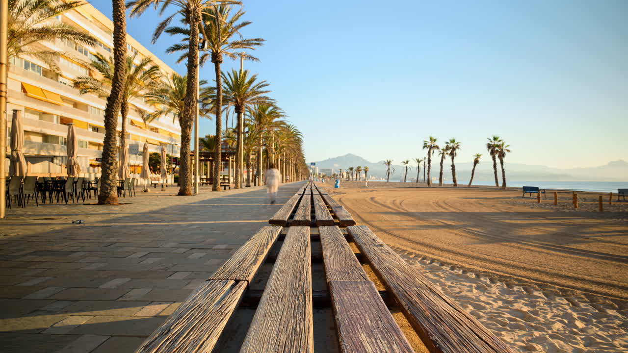 Time lapse di persone che camminano su una passeggiata fiancheggiata da palme vicino alla spiaggia all'alba ad Alicante, Spagna