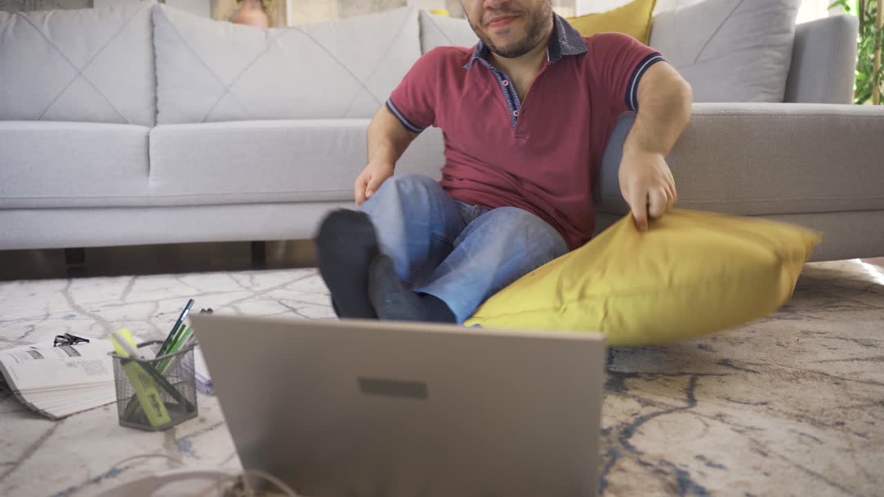 un joven enano feliz y alegre acostado en el suelo usando una computadora portátil en casa.