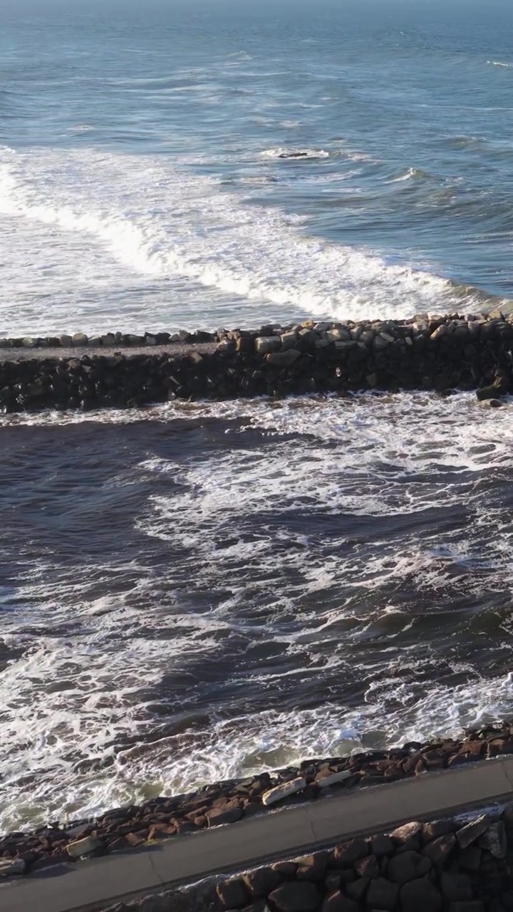 Onde oceaniche dinamiche si infrangono contro un frangiflutti roccioso sotto cieli sereni a Brunswick Heads, NSW, Australia.