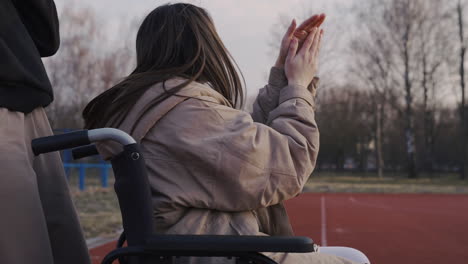 Mujer-Discapacitada-En-Silla-De-Ruedas-Y-Su-Amiga-Animando-Y-Aplaudiendo-A-Sus-Amigos-Que-Juegan-Baloncesto