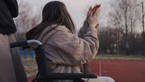mujer discapacitada en silla de ruedas y su amiga animando y aplaudiendo a sus amigos que juegan baloncesto
