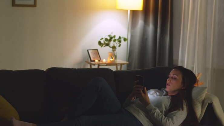 Woman Lying On Sofa At Home At Night Streaming Or Looking At Online Content On Mobile Phone 3