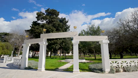 an elegant white arch with columns in a public park in pafos, surrounded by green grass and trees