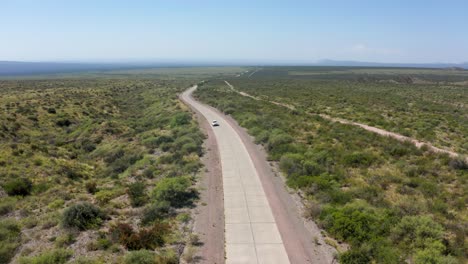 Un-Solo-Coche-Blanco-Que-Viaja-Por-Un-Camino-Estrecho-Y-Largo-En-Un-Vasto-Desierto-árido