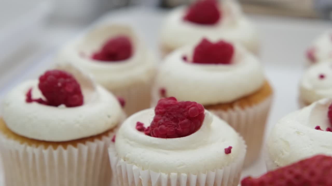 Delicious muffins on tray with white icing and raspberries.