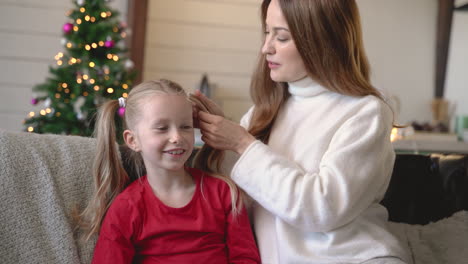 mother and daughter sitting on the sofa covered by a blanket while talking in living room with christmas decorations 3