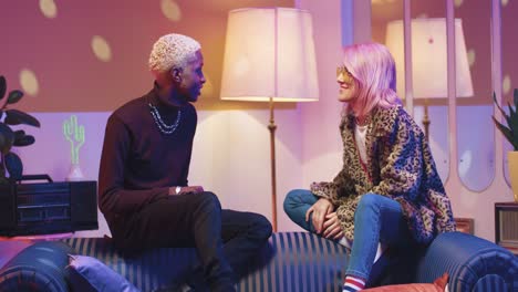 african american man and caucasian stylish woman in sunglasses dancing and talking while sitting on couch in a retro party at home