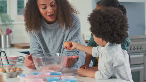 mother and children in kitchen mixing ingredients together for cupcakes