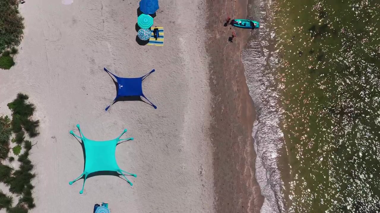 Tende e ombrelloni nelle tonalità verde acqua e blu brillante costeggiano una spiaggia sabbiosa accanto a onde leggere, visti direttamente dall'alto