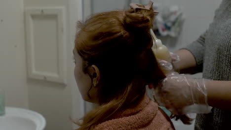 estilista de cabello usando guantes aplicando tinte de cabello de la botella al cabello del cliente en casa en el baño