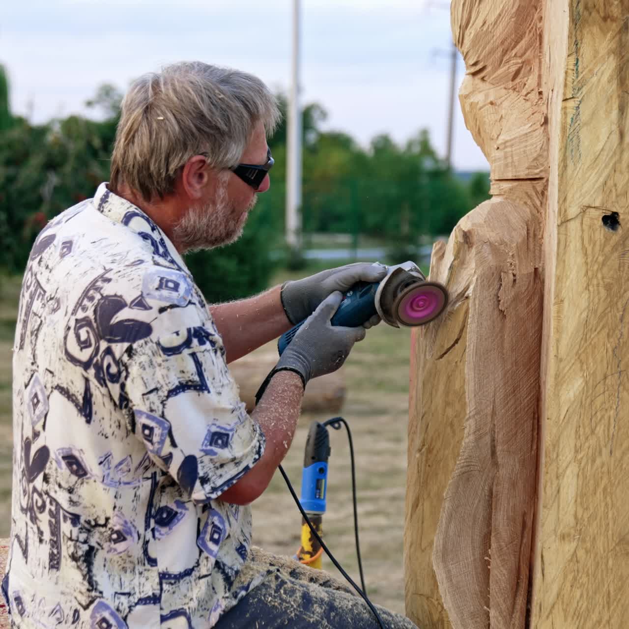 Adult Caucasian man making a wooden sculpture. Artist uses electric instrument in his work