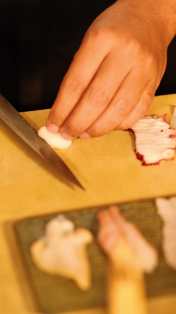 Close-up of chef hands using sharp knife to slice raw octopus for sashimi in Bangkok.