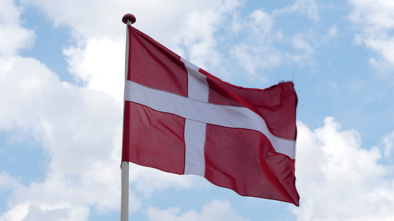 Dansk flag vajende på blæsende dag mod himmel med skyer