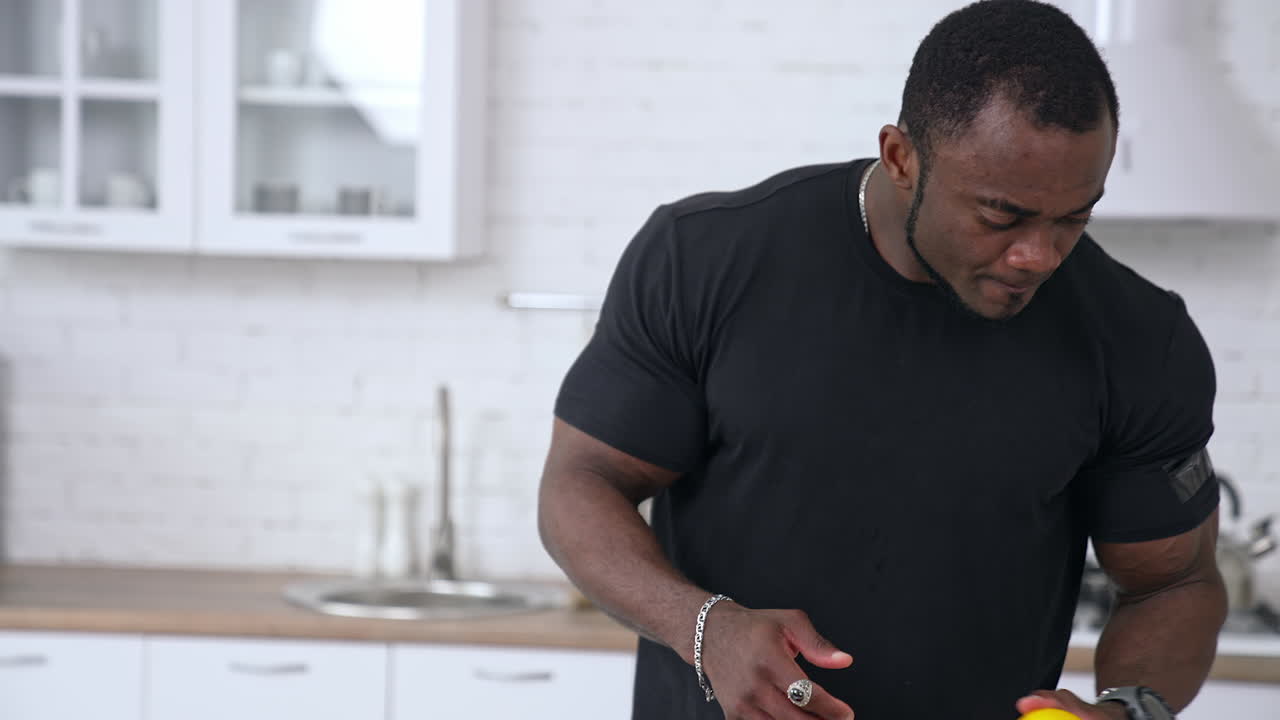 Healthy african man in the kitchen. Handsome black man in black t-shirt with muscular body cooking food with fresh vegetables.
