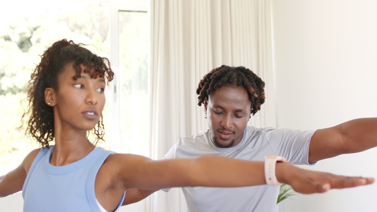 African couple performing arm stretch after man's cue in living room, checking form with smartwatch