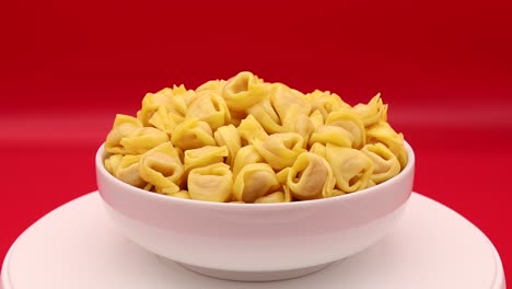tortellini crudo girando sobre un fondo rojo