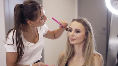 The-make-up-artist-applies-the-powder-to-finish-client's-makeup-at-bright-studio