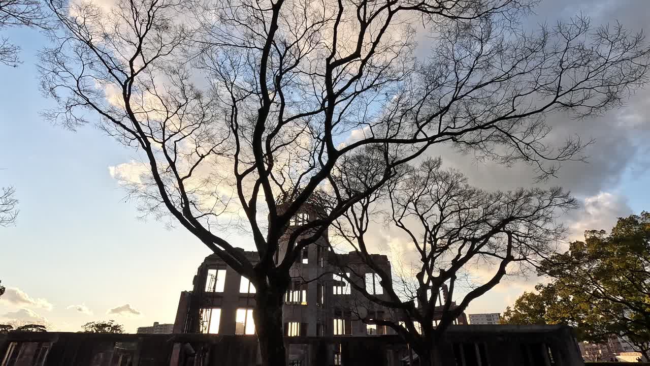 The Hiroshima Peace Memorial Dome in silhouette during sunset, framed by bare winter trees and a glowing sky in Hiroshima, Japan—an emotional view of this historic World Heritage Site.