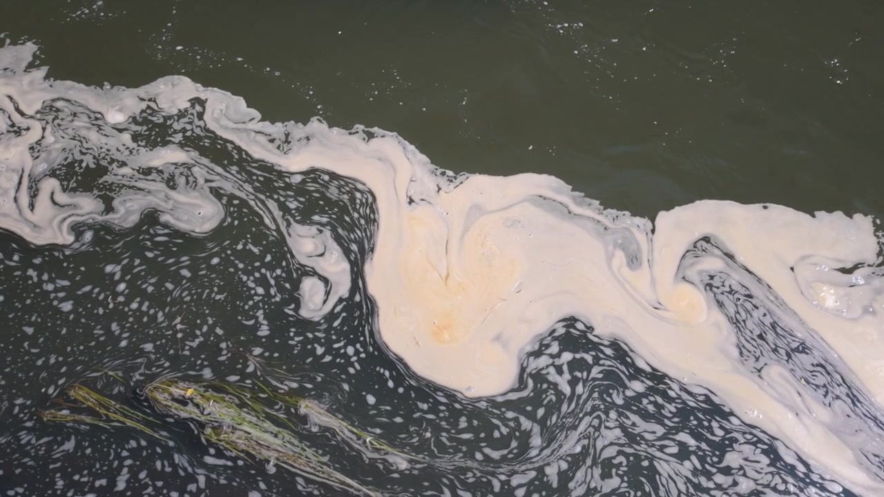 Abstract dark water surface with swirling white foam and soft oily patterns, creating a natural texture background