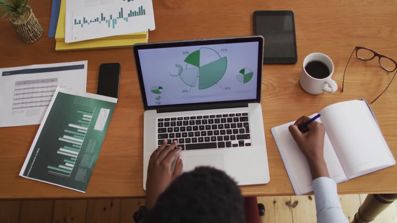 vista aérea de una mujer afroamericana usando una computadora portátil y tomando notas mientras trabaja desde casa