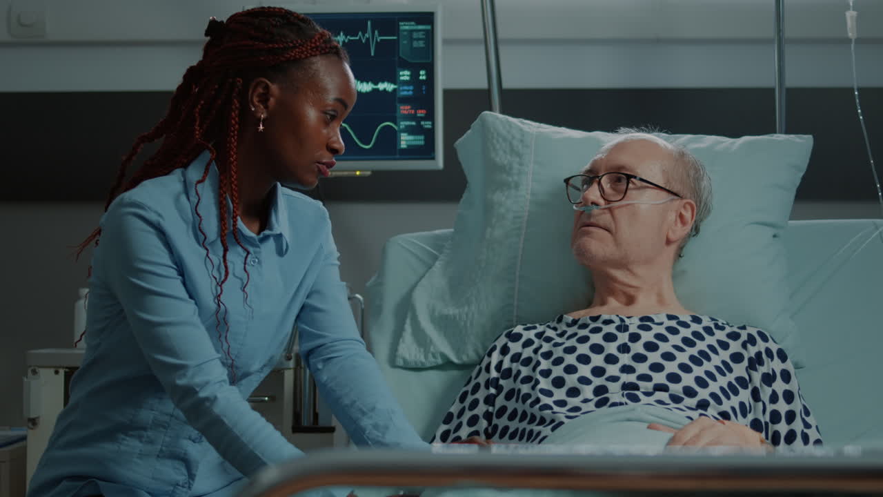 Sick elder patient laying in bed talks to african american visitor