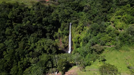 Panning-wide-drone-perspective-of-tall-waterfall-surrounded-by-rainforest-green-vegetation,-Monte-verde