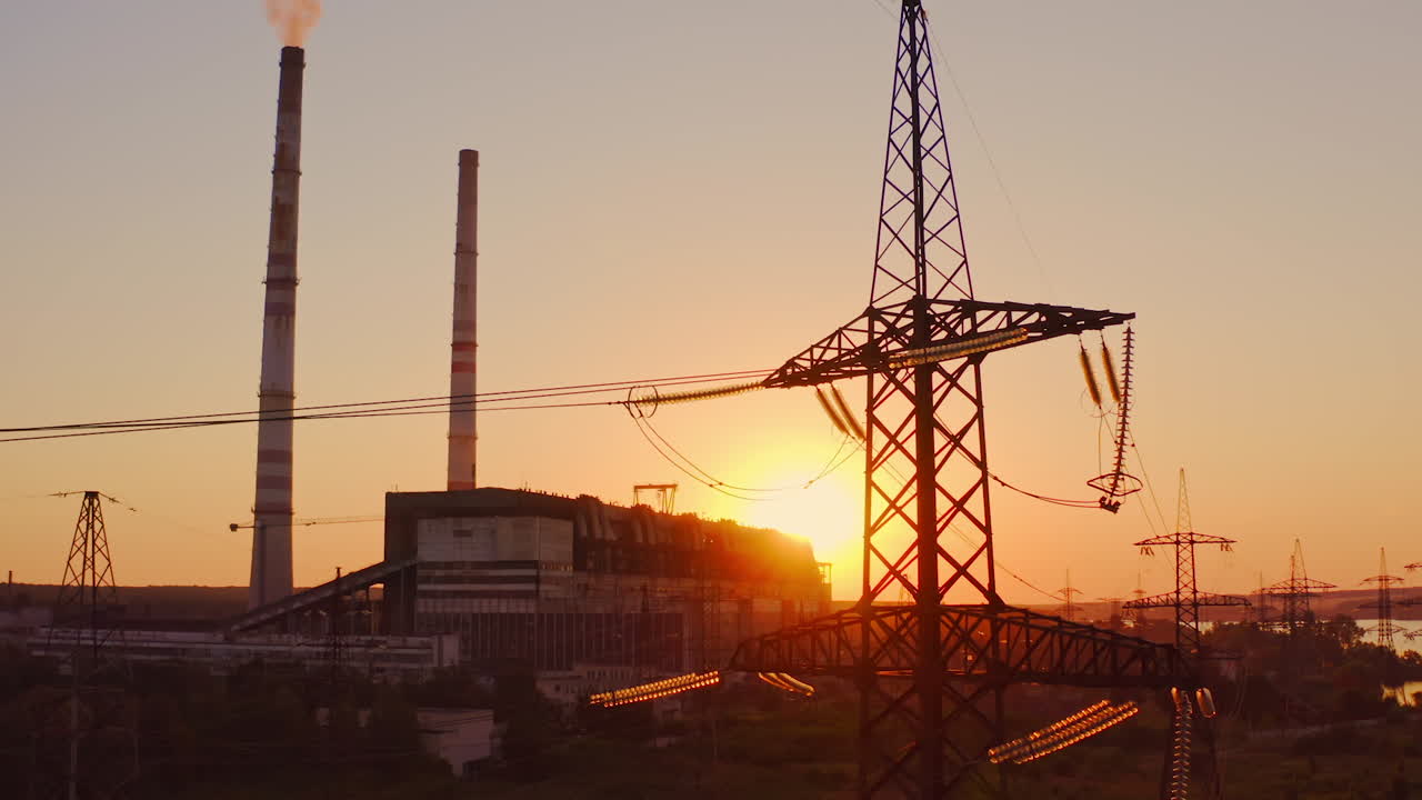 Industrial high voltage electricity tower. Silhouette of high voltage electric tower on sunset time. Industrial factory against the evening sky on sunset time background.