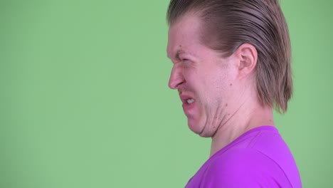 zoom in shot of young man profile view looking disgusted against green background