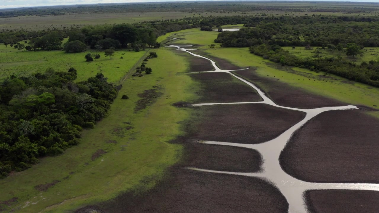 Aerial footage captures the vast, winding channels of a low-water river cutting through green savanna wetlands in Colombia’s Orinoquía region under dramatic cloudy skies.
