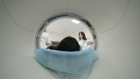la paciente está siendo sometida a una tomografía computarizada o resonancia magnética bajo la supervisión de un radiólogo en una clínica médica moderna. la paciente está acostada en una cama de tomografía computorizada o resonanza magnética, moviéndose dentro de la máquina.