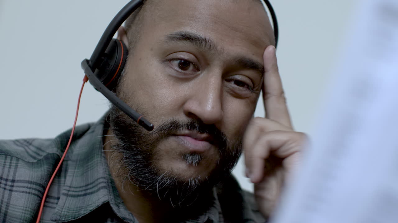 destacado hombre asiático del reino unido usando auriculares trabajando desde casa asintiendo con la cabeza mirando las facturas