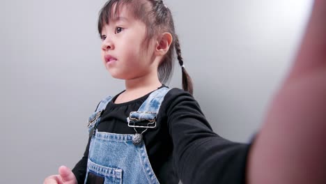 happy little asian girl using a smartphone for video call, waving hand and speaking and talking with a smile greeting teacher and classmates