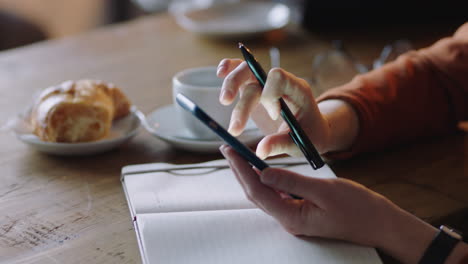 close up business woman hands using smartphone in cafe drinking coffee texting reading email messages writing notes brainstorming ideas enjoying busy restaurant