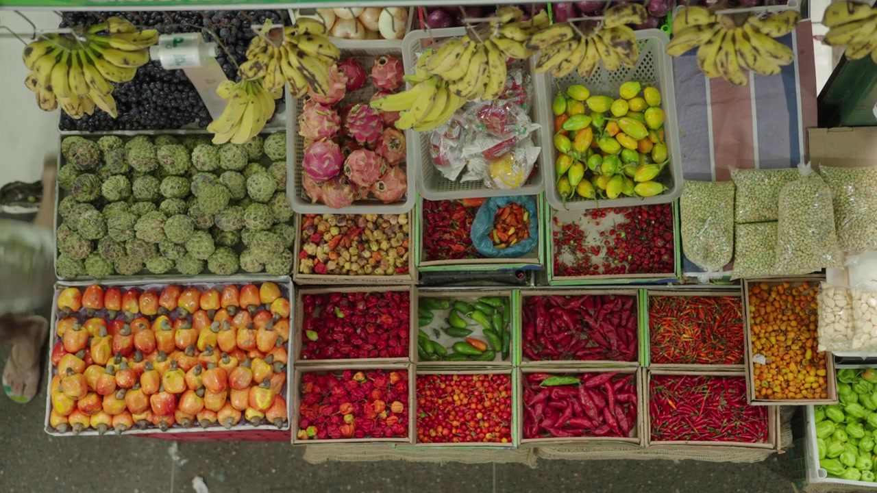 Frutas tropicais variadas e pimentões cuidadosamente organizados em caixas em uma barraca de feira livre