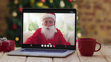 senior caucasian man in santa costume on video call on laptop, with christmas decorations and tree