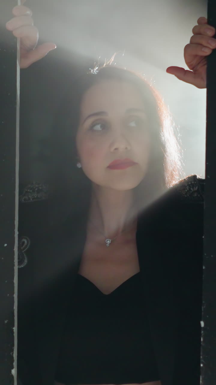 mujer enigmática en traje negro enmarcada por una puerta, suavemente iluminada por la luz de fondo a medida que la cámara hace zoom