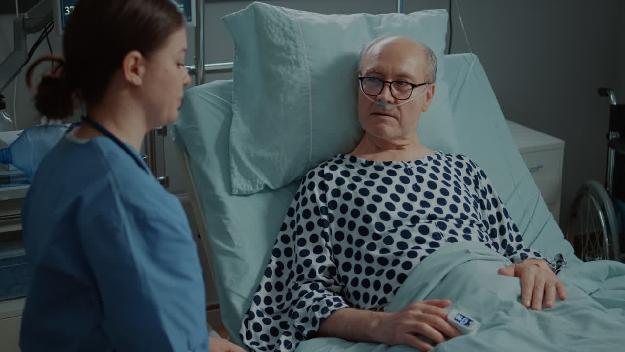 Sick old patient getting help from nurse in hospital ward