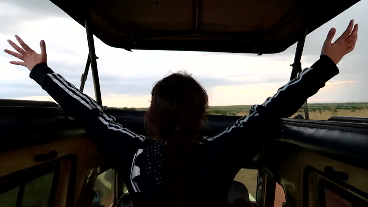 feliz mujer entusiasta levanta los brazos mientras está de pie en un coche safari 4x4, vista trasera